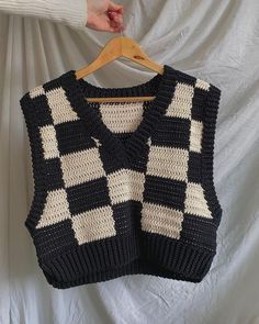 a black and white knitted sweater hanging on a wooden hanger with a person's hand