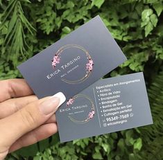 someone holding up two business cards in front of some bushes and trees with pink flowers on them