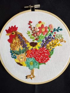 an embroidered rooster with flowers on it's back is sitting in front of a black background