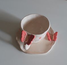 a white cup and saucer with two pink butterflies on it sitting on a plate