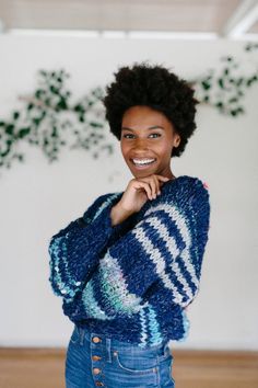 a smiling woman in a blue sweater and jeans stands with her arms on her chest