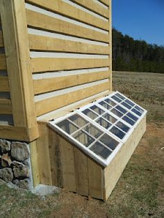 a small window on the side of a wooden building with grass and rocks around it