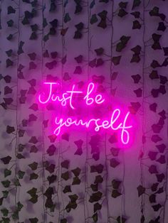 a neon sign that says, just be yourself on the side of a wall covered in ivy