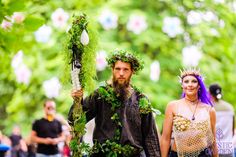 a man and woman dressed up in costume walking down the street with flowers on their heads