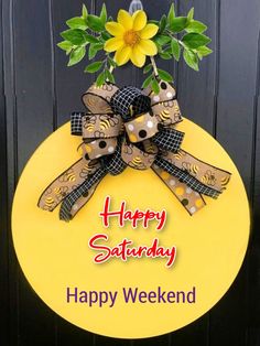 a yellow happy saturday sign hanging on a black wooden door with a flower in the center