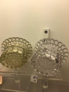 two glass dishes sitting on top of a clear shelf next to each other in front of a white wall