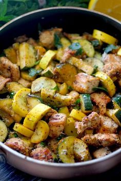 a pan filled with potatoes and meat on top of a table next to lemon wedges