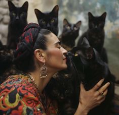 a woman kissing a black cat with many cats behind her