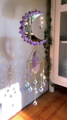 a purple and white wind chime hanging from a wall next to a window with light shining on it