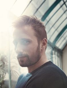 a man in black shirt standing next to a building and looking at the camera with light coming through his eyes