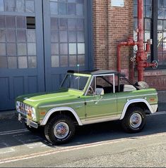 a green pick up truck parked in front of a brick building next to a red fire hydrant