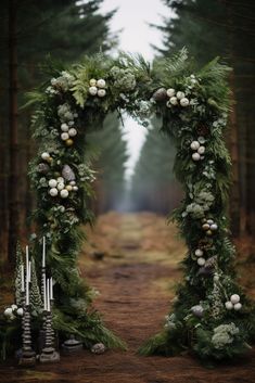 an arch made out of greenery and candles stands in the middle of a forest