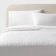 a bed with white sheets and pillows on top of it, next to a headboard