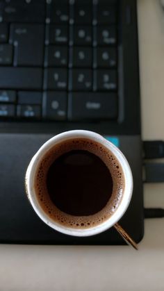 a cup of coffee sitting in front of a laptop computer