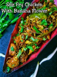 stir fry chicken with banana flower served in a boat on a blue tablecloth next to green onions and cilantro