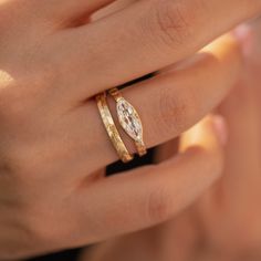 a woman's hand with two gold rings on her left and the ring has an oval shaped diamond in it