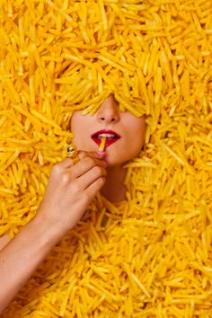 a woman with red lipstick is surrounded by yellow shredded noodles as she holds a ring