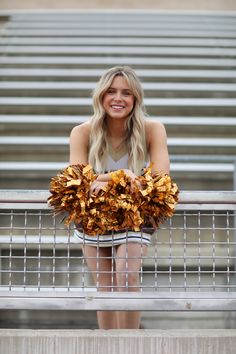 a beautiful young blond woman sitting on top of a metal railing holding a cheerleader's pom - pom