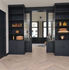 an empty room with black bookshelves and wooden floors in the center is filled with vases