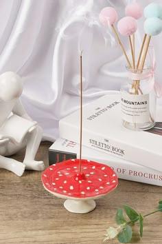 a table topped with books and candles next to a vase filled with pink, white and blue pom poms