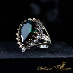 a ring with an oval shaped green stone surrounded by small white diamonds on a black surface