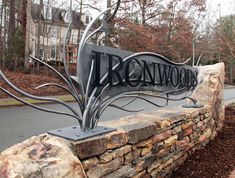 a large metal sign sitting on the side of a road next to a stone wall