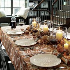 a table set with plates, candles and wine glasses on it in front of a spiral staircase