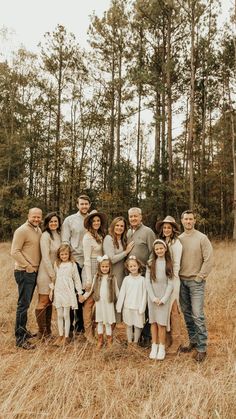 a large family is posing for a photo in the grass with tall trees behind them