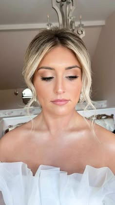 a woman in a white dress is looking down at her wedding day hair and makeup