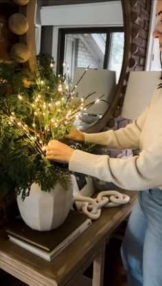 a woman is decorating a christmas tree in her living room with lights on the branches