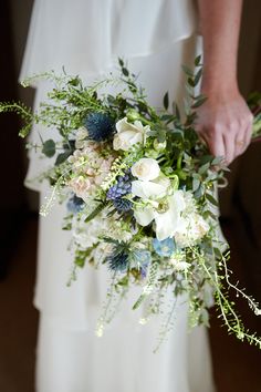 a bride holding a bouquet of flowers and greenery