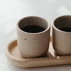 two coffee cups sitting on top of a wooden tray