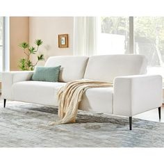 a white couch sitting on top of a rug in a living room next to a window