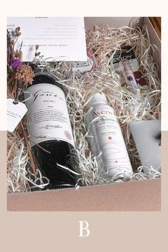 three bottles of wine in a box with some flowers and papers on the table next to it