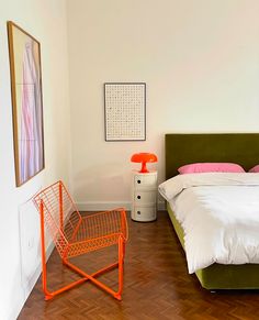 a bed room with a neatly made bed and an orange chair next to the bed