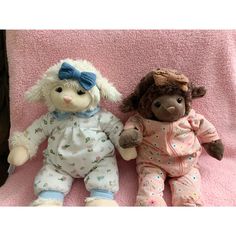 two stuffed animals laying on top of a pink blanket next to each other in pajamas