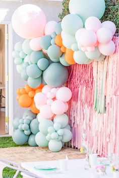 the balloon wall is decorated with pastel colors and tassels for an outdoor party