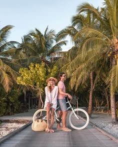 two people standing on a pier with their bikes in front of them and palm trees behind them