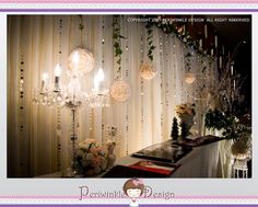 a table with flowers and candles on it in front of a curtained wall that has lights hanging from it