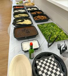 an assortment of food is laid out on a long table with plates and utensils