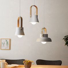 three lights hanging from the ceiling above a table with chairs and a potted plant