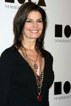 a woman in black shirt and necklace smiling at the camera with her hand on her hip