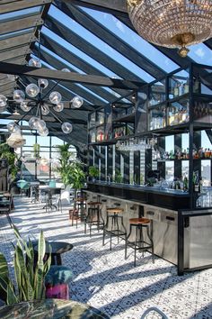 an outdoor bar with several stools and tables under a glass roof over looking the ocean