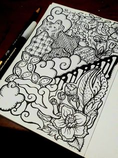 a coloring book with flowers and other things on the page, next to a pen