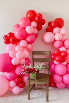 Two organic balloon arches frame a brown wooden chair. The balloon garland is made up of red, pink and rose colored balloons of varying sizes. A floral arrangement sits on the chair, long white stems with white flowers and rose-like red flowers make up the arrangement. The set up is Valentines themed. Red Balloon Arch, Valentines Balloons Decorations, Red Baby Shower, Red Party Decorations, Baby Shower Balloon Arch, Valentines Birthday Party, Red Birthday Party, Valentines Party Decor, Rose Colors