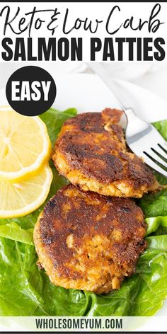 two salmon patties on top of lettuce with lemon wedges and a fork