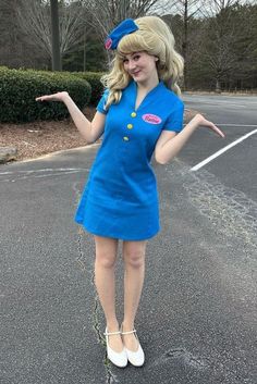 a woman in a blue dress is standing on the street with her hand out to someone