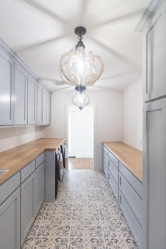 an empty kitchen with grey cabinets and white walls, light fixture in the middle is hanging from the ceiling