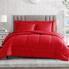 a bed with red comforter and pillows in a room next to a white brick wall