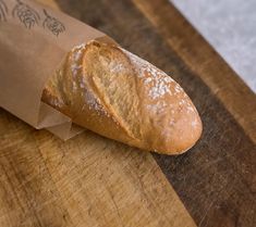 a piece of bread sitting on top of a wooden cutting board next to a paper bag